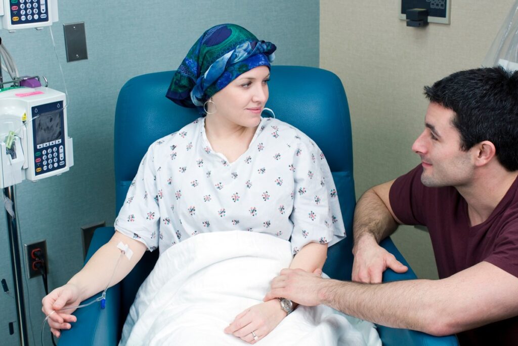 Paciente com câncer de mama recebendo quimioterapia acompanhada pelo marido em ambiente hospitalar.