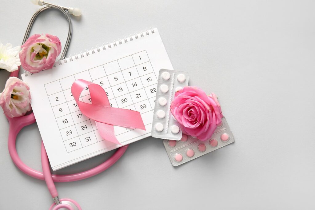 Composição de capa para artigo sobre anticoncepcionais e câncer de mama com laço rosa, pílulas e calendário em fundo cinza.