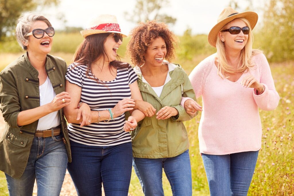Grupo de mulheres maduras caminhando e sorrindo em parque, simbolizando qualidade de vida e amizade.