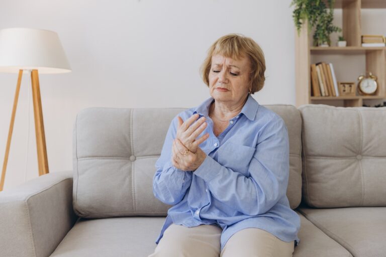 Mulher idosa segurando as mãos com expressão de dor articular, representando um dos efeitos colaterais mais comuns da hormonioterapia para câncer de mama